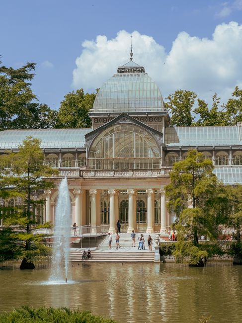 The image features the Temperate House, a large historic glasshouse with a domed roof, situated in a landscaped park setting. The structure is constructed with a metal framework and extensive glass pa